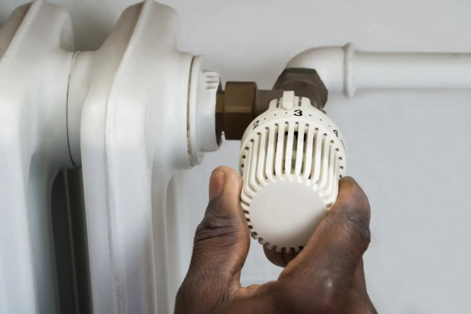 En hånd drejer på en hvid termostat på en radiator